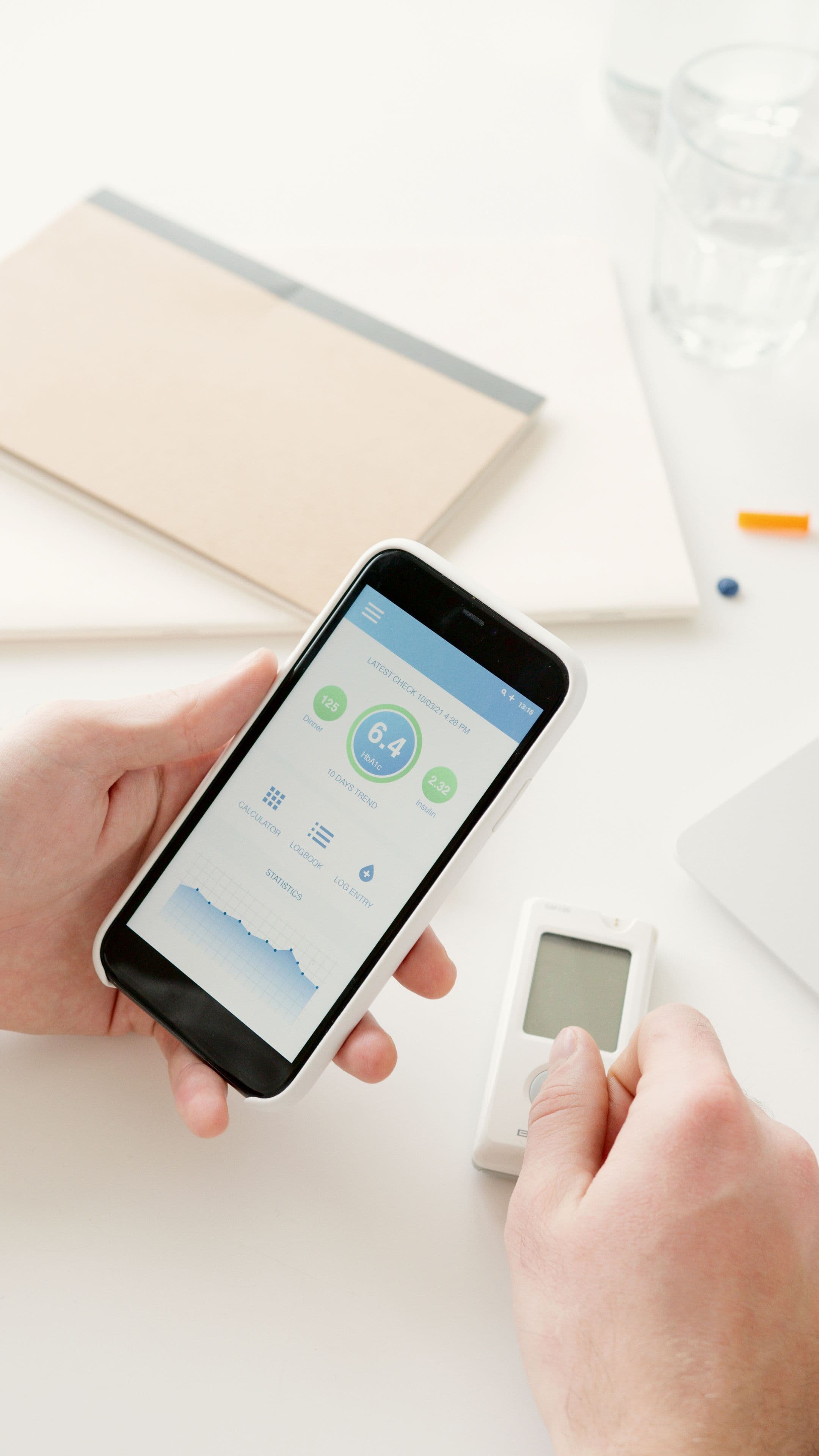 Hand hält ein Smartphone mit einer Gesundheits-App neben einem Blutzuckermessgerät