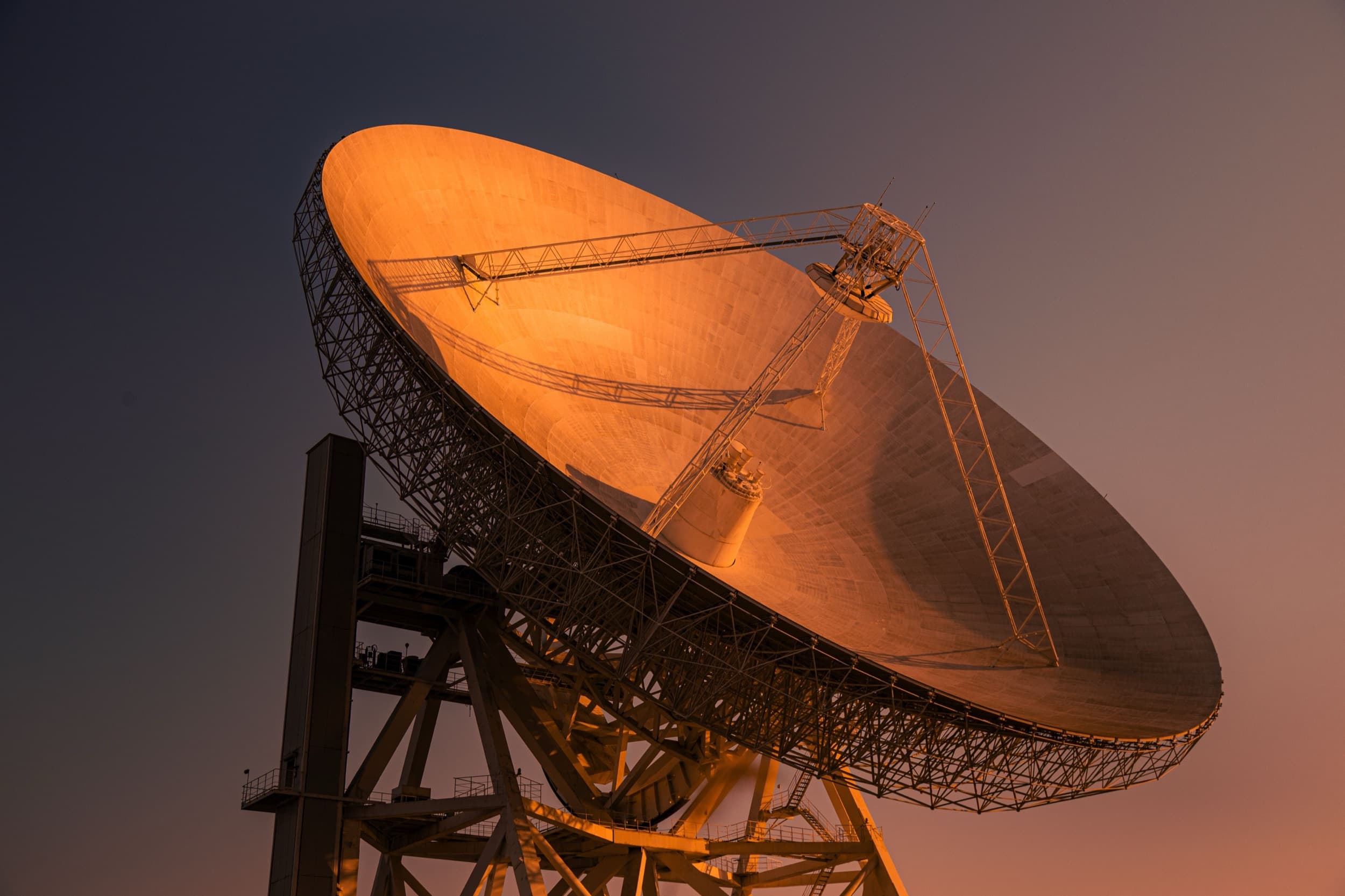 Große Radioteleskop-Schüssel im orangefarbenen Abendlicht vor dunkelblauem Himmel