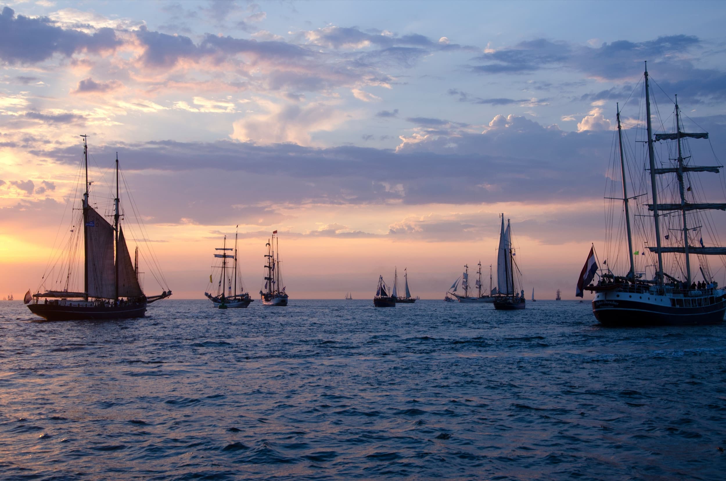Flotte aus Traditionsseglern und Großseglern auf offener See im Sonnenuntergang