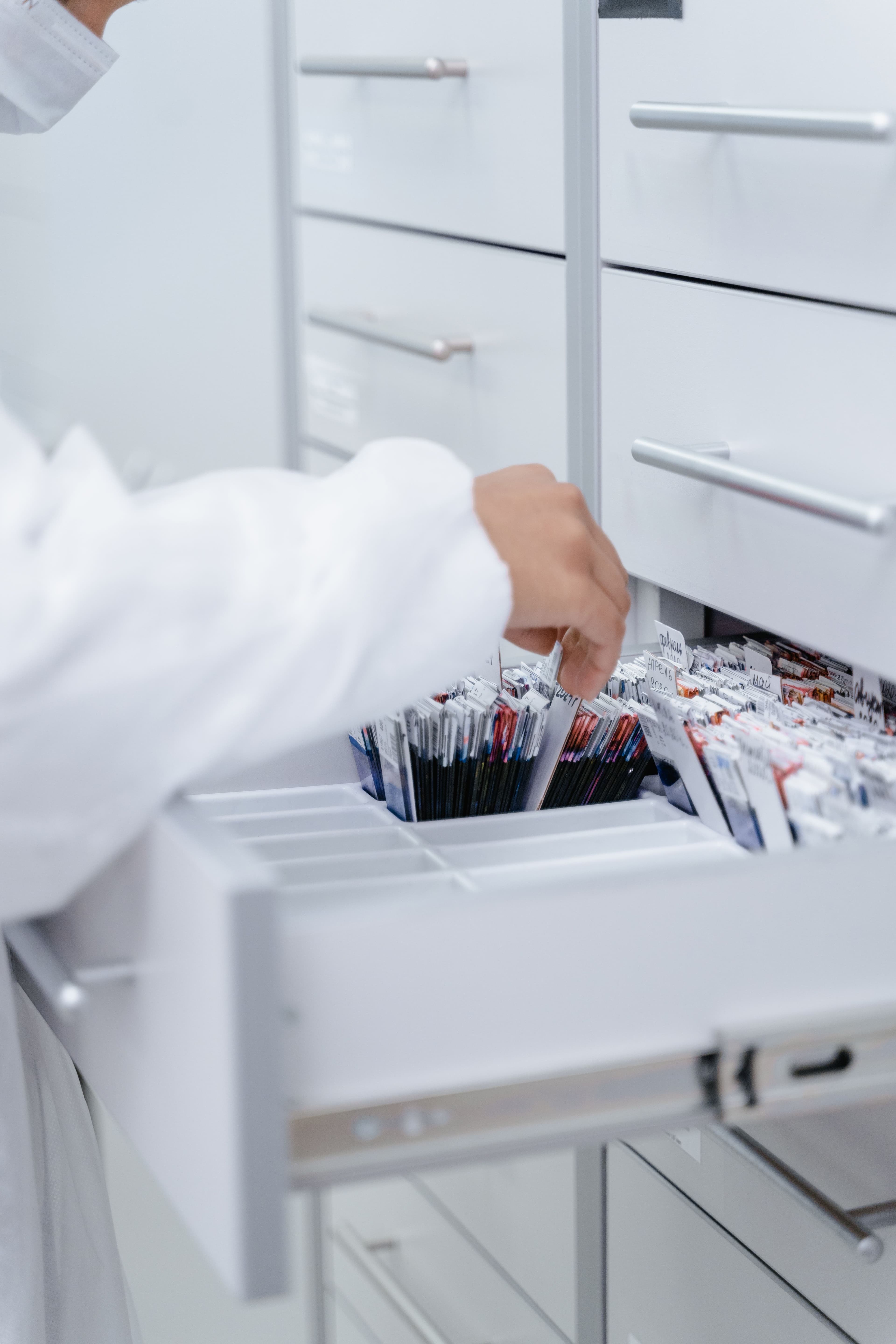 Person im weißen Kittel zieht eine Patientenakte aus einer Aktenschublade
