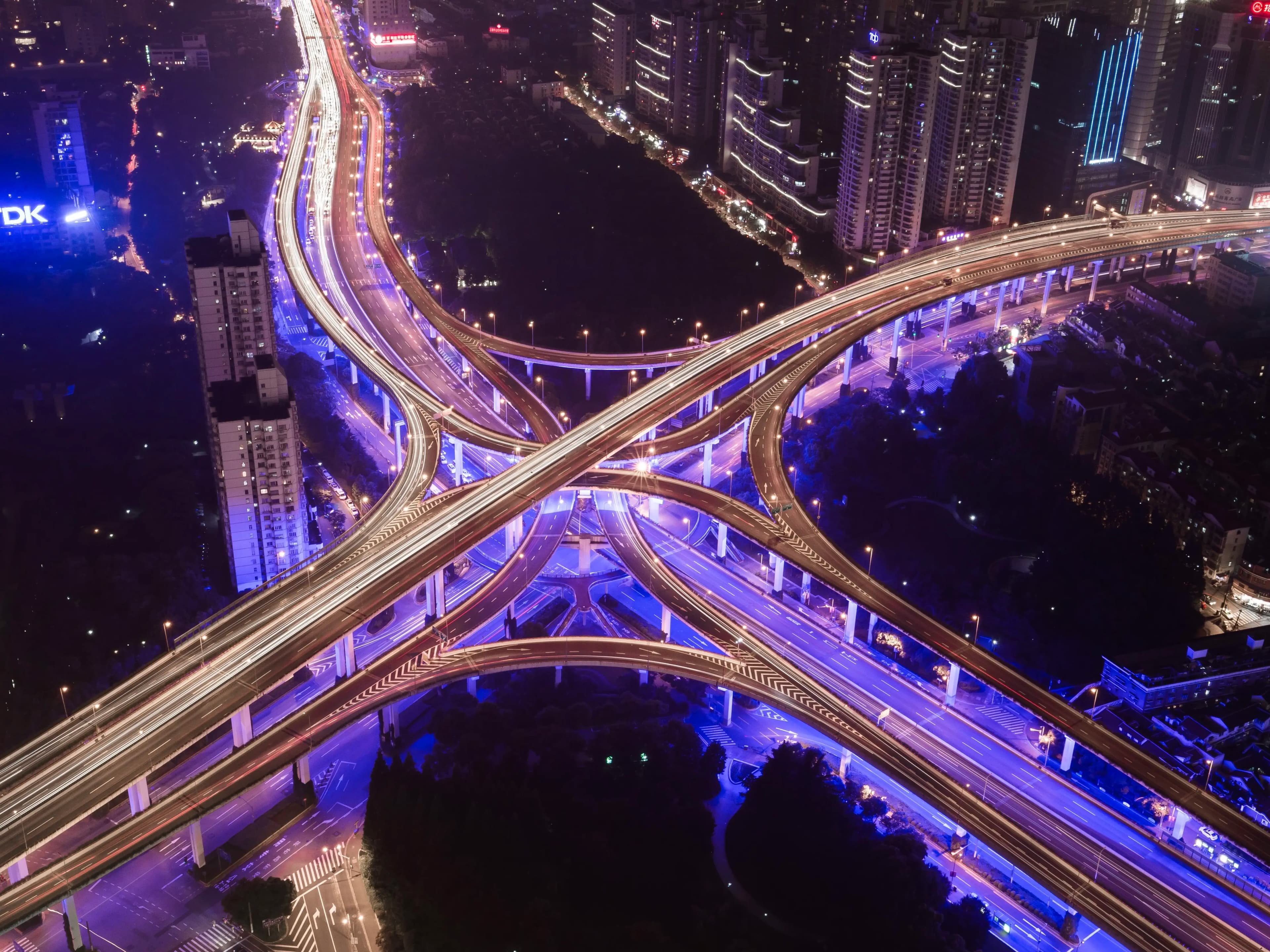 Beleuchtete Autobahnkreuzung bei Nacht mit Skyline im Hintergrund