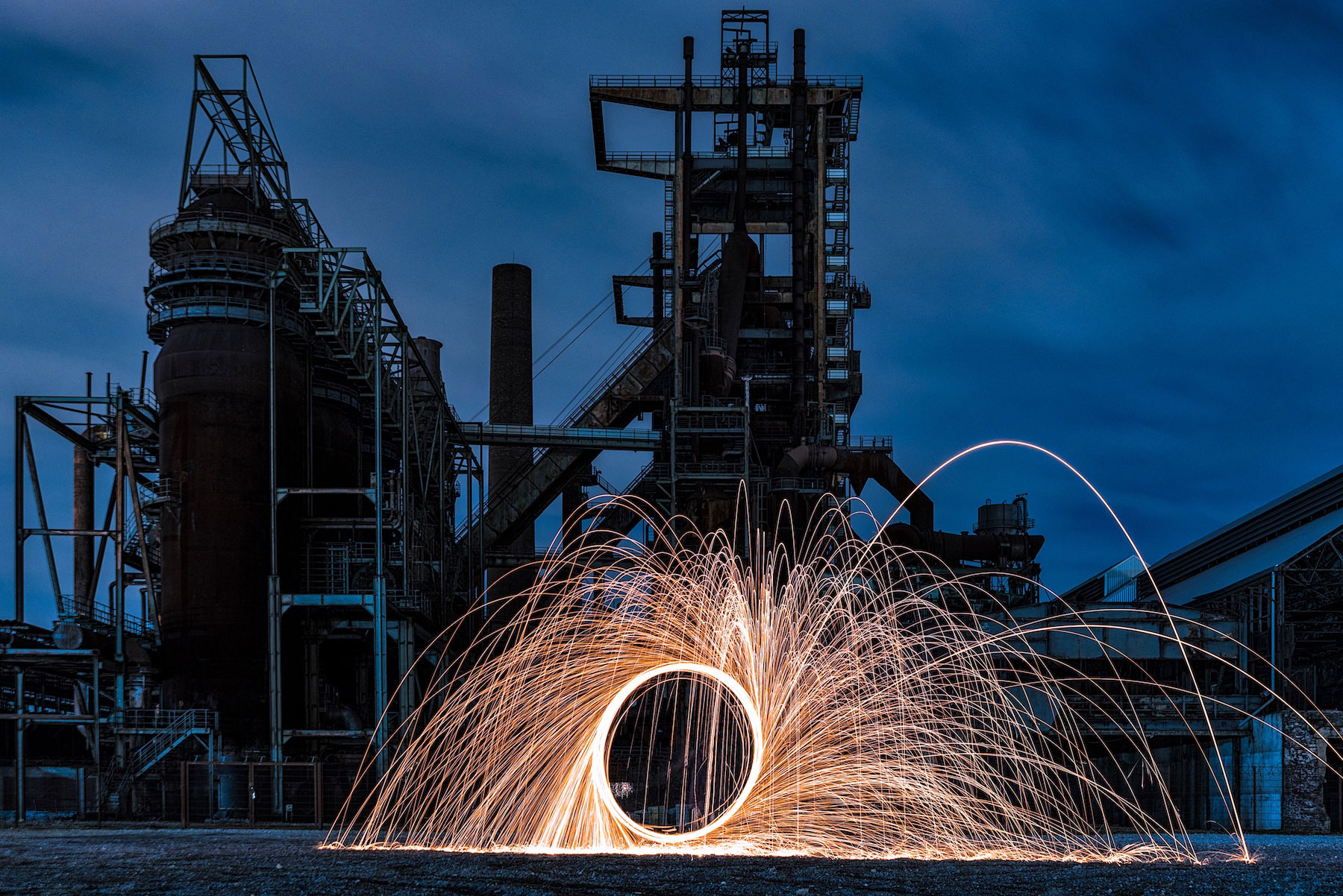 Eiine Person steht auf einem Jeep und bildet aus Funken einen Kreis. Die Funken sprühen im großen Bogen nach außen. Es ist Nacht. Die Funken sind Maskottchen von sparqs und deren Leistungen.