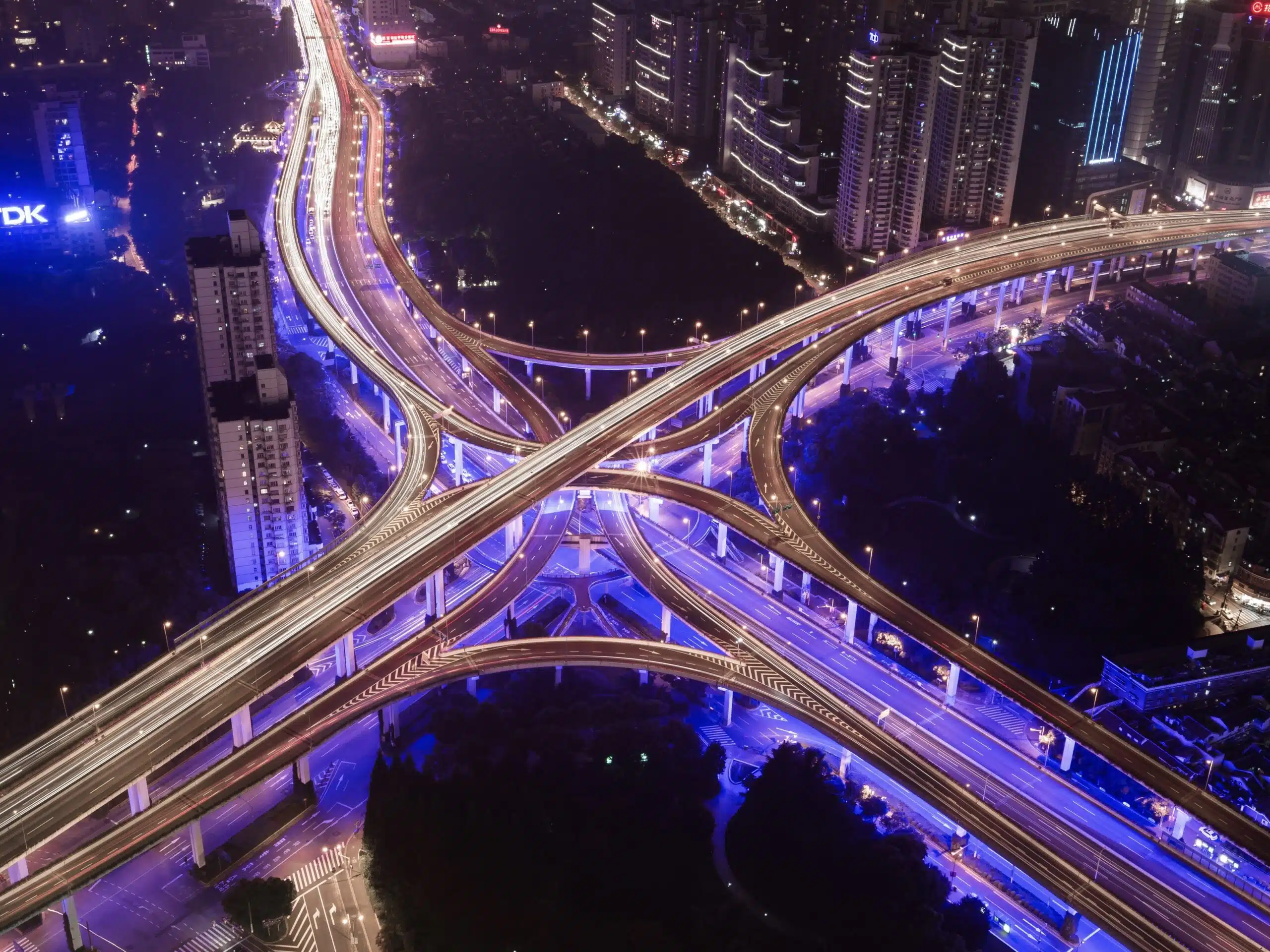 Cityscape and interchange Aus der Vogelperspektive wird ein Highway bei Nacht gezeigt. Die Lichter sind aufgrund der Geschwindigkeit verschwommen. Diese Dynamik drücken auch die Digital Business Solutions aus